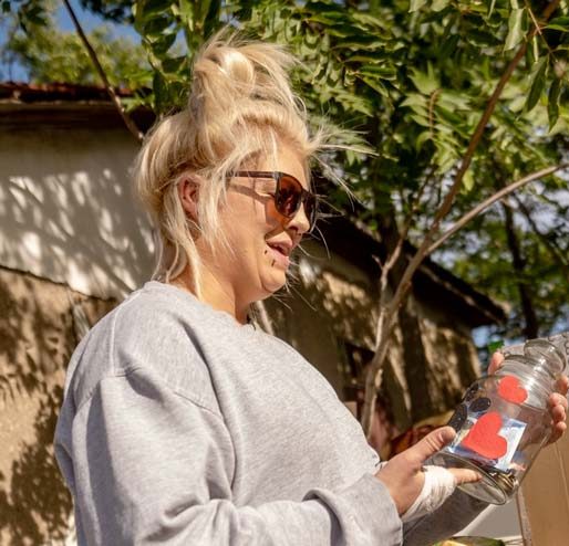 Eine Person mit Sonnenbrille kniet und spielt mit zwei Welpen, einem schwarzen und einem weißen.
