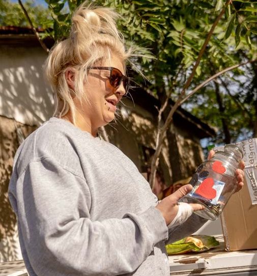 Eine Person mit Sonnenbrille kniet und spielt mit zwei Welpen, einem schwarzen und einem weißen.