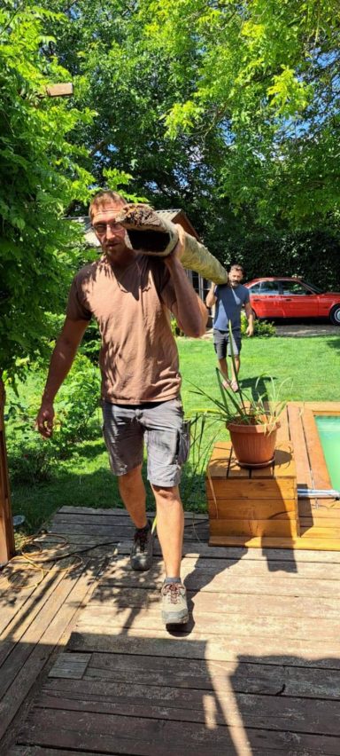 Mann trägt eine Holzplatte, während eine andere Person im Hintergrund beobachtet.